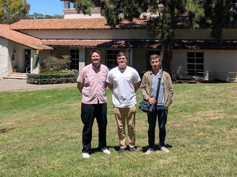 group photo, 3 dudes standing in front of a library on a grass lawn